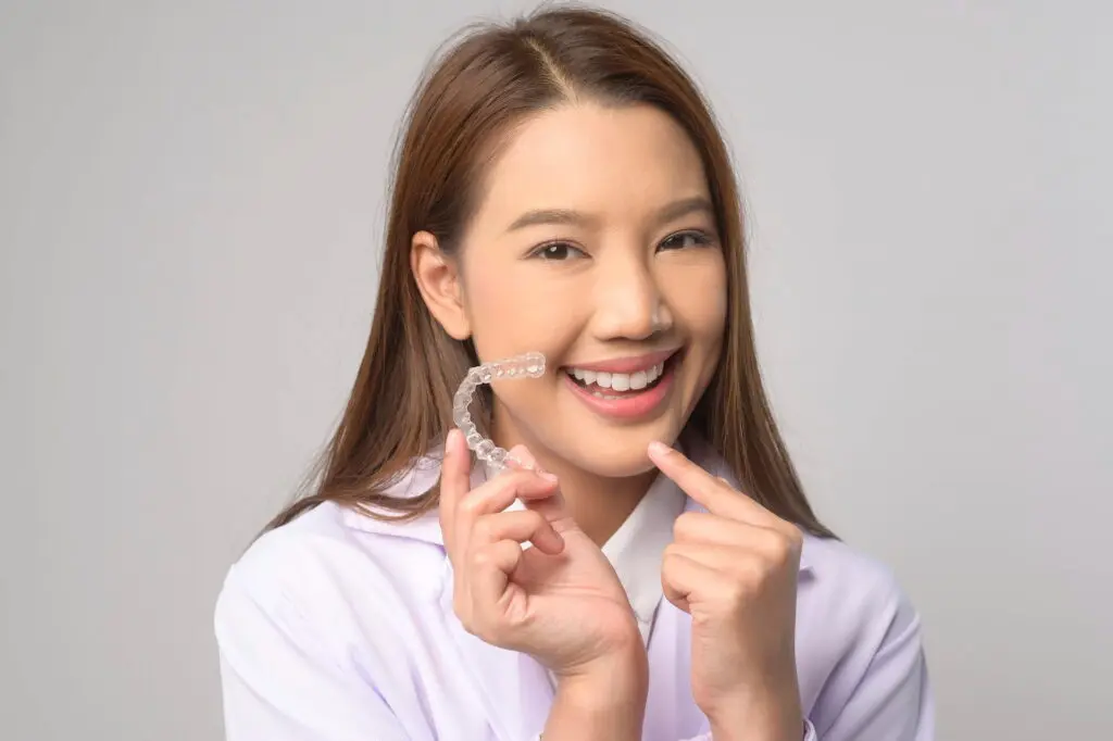 A woman stands confidently, holding a invisalign in her hand, ready for her dental care routine in Austin, TX