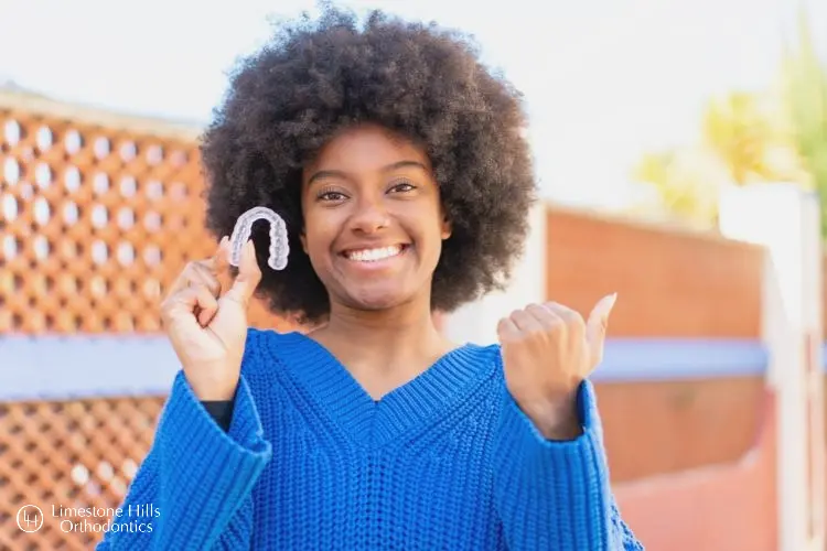 a girl posing with her thumb up and holding Invisalign. How Does Invisalign Work? 