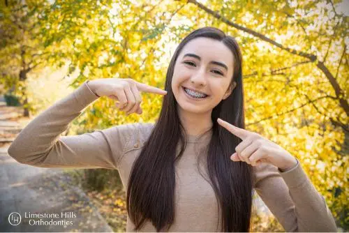 a girl pointing at her teeth with Invisalign vs Braces Cost