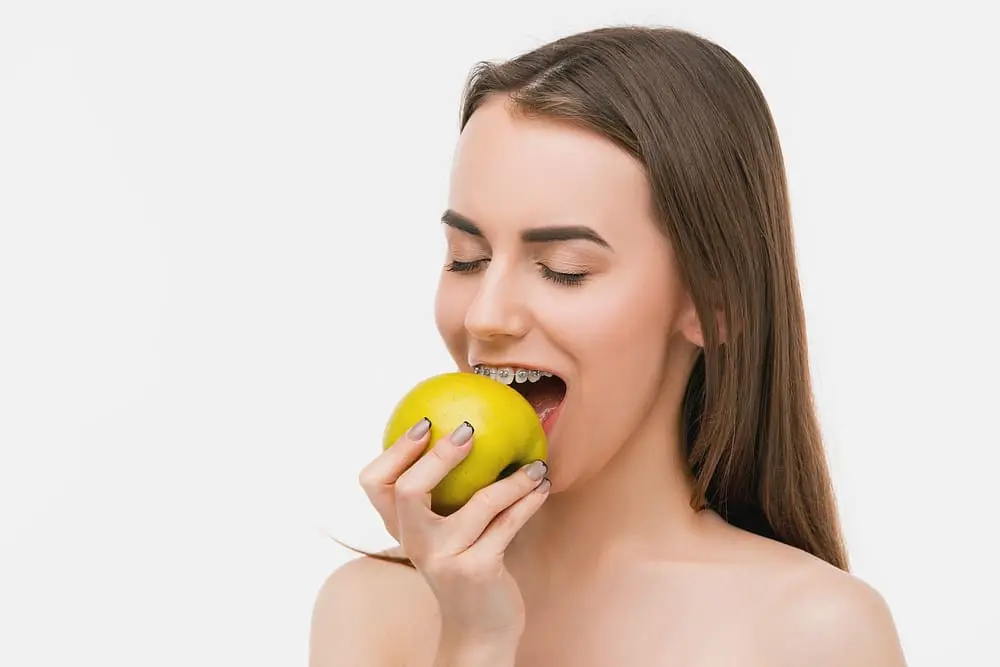 Beautiful young woman with metal braces smiling and biting an apple after knowing how to remove food from braces