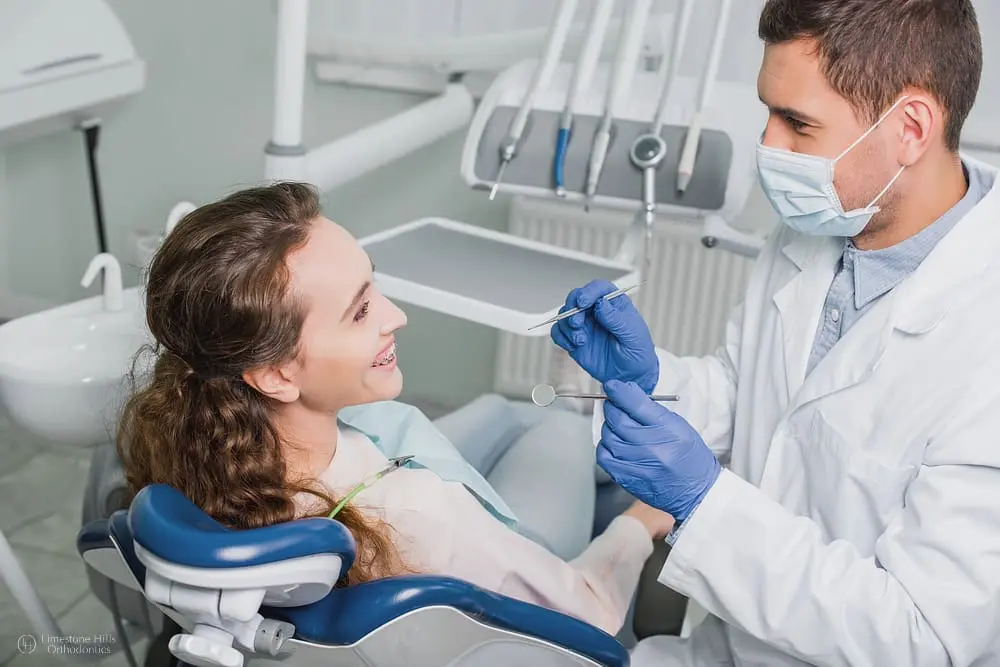 At Limestone Hills Orthodontics in Austin, TX, a dentist with gloves and mask discusses treatment with a smiling patient in a chair.