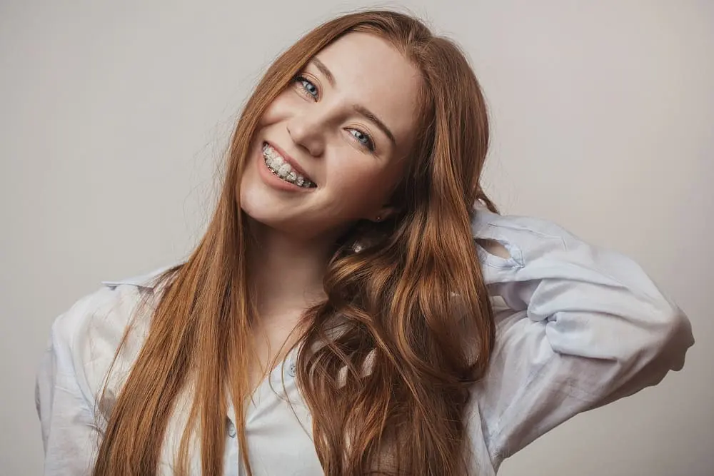Happy young red-haired woman smiling with adult clear braces after she is free from risks of mail order orthodontics in in Austin, TX