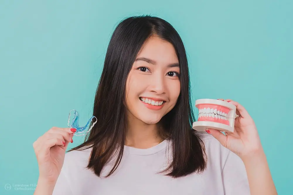 Young Asian woman smiling and holding a silicone orthodontic retainer to illustrate what happens when your retainer doesn't fit.
