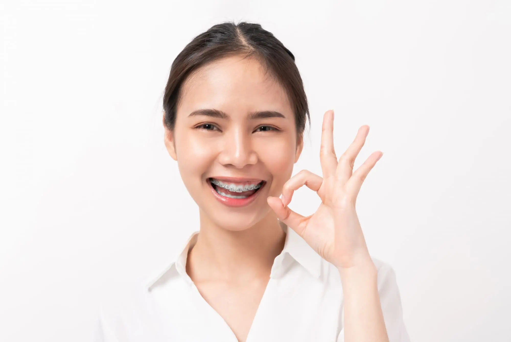 Smiling woman with ceramic braces making an OK sign at Limestone Hills Orthodontics in Austin, TX.