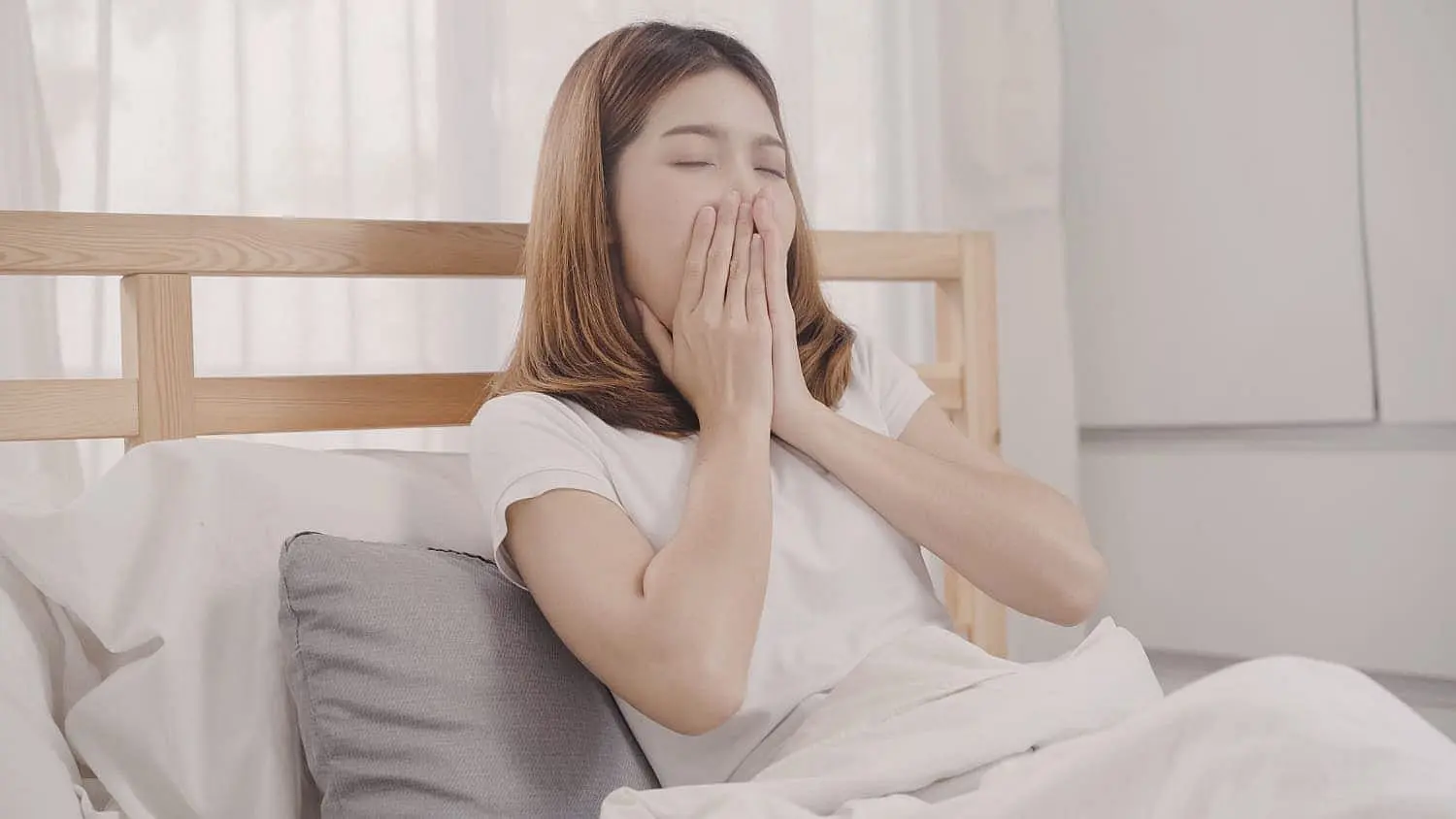 A tired woman yawns in bed, likely after snoring; Limestone Hills Orthodontics in Austin, TX offers airway appliances.