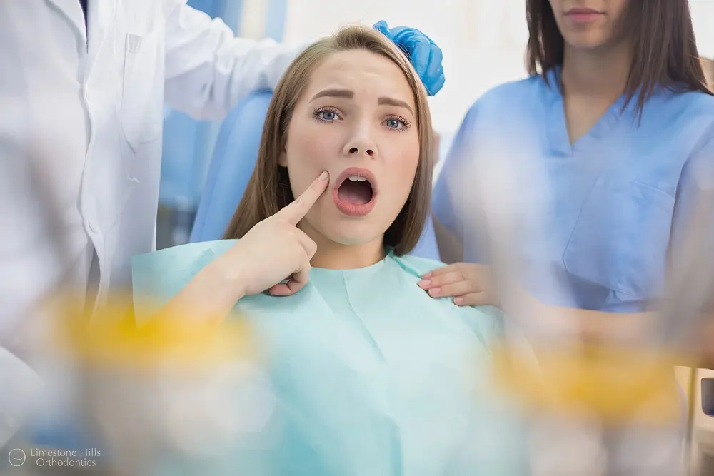 At Limestone Hills Orthodontics in Austin, TX, a concerned woman in a dental chair points to her mouth as the dentist explains underbite risks.