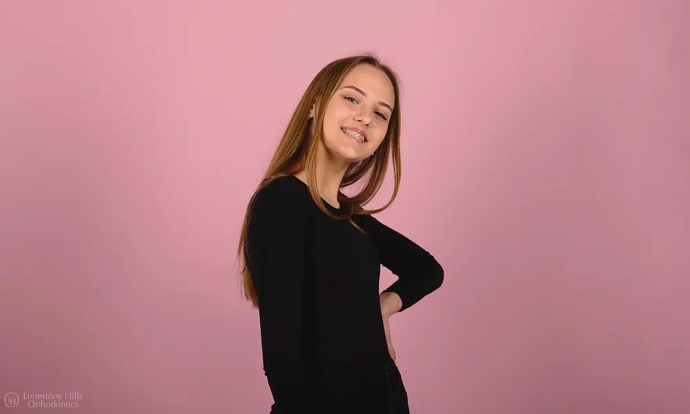happiness facial expressions woman smile wears metal braces teeth pink - Why Your Child Should Have Two-Phase Orthodontic Treatment in Austin, TX