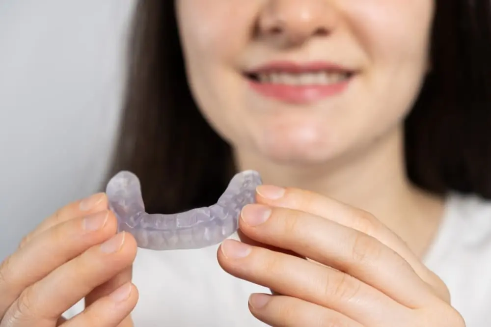 At Limestone Hills Orthodontics in Austin, TX, a person holds a clear dental aligner in both hands, partial smile in view.