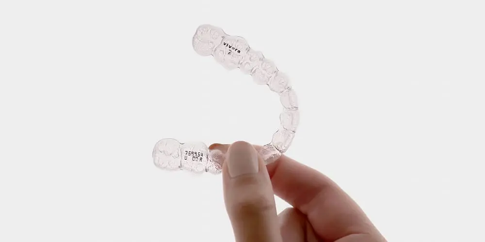 A hand holds a Vivera Retainer from Limestone Hills Orthodontics in Austin, TX, with a plain white background.